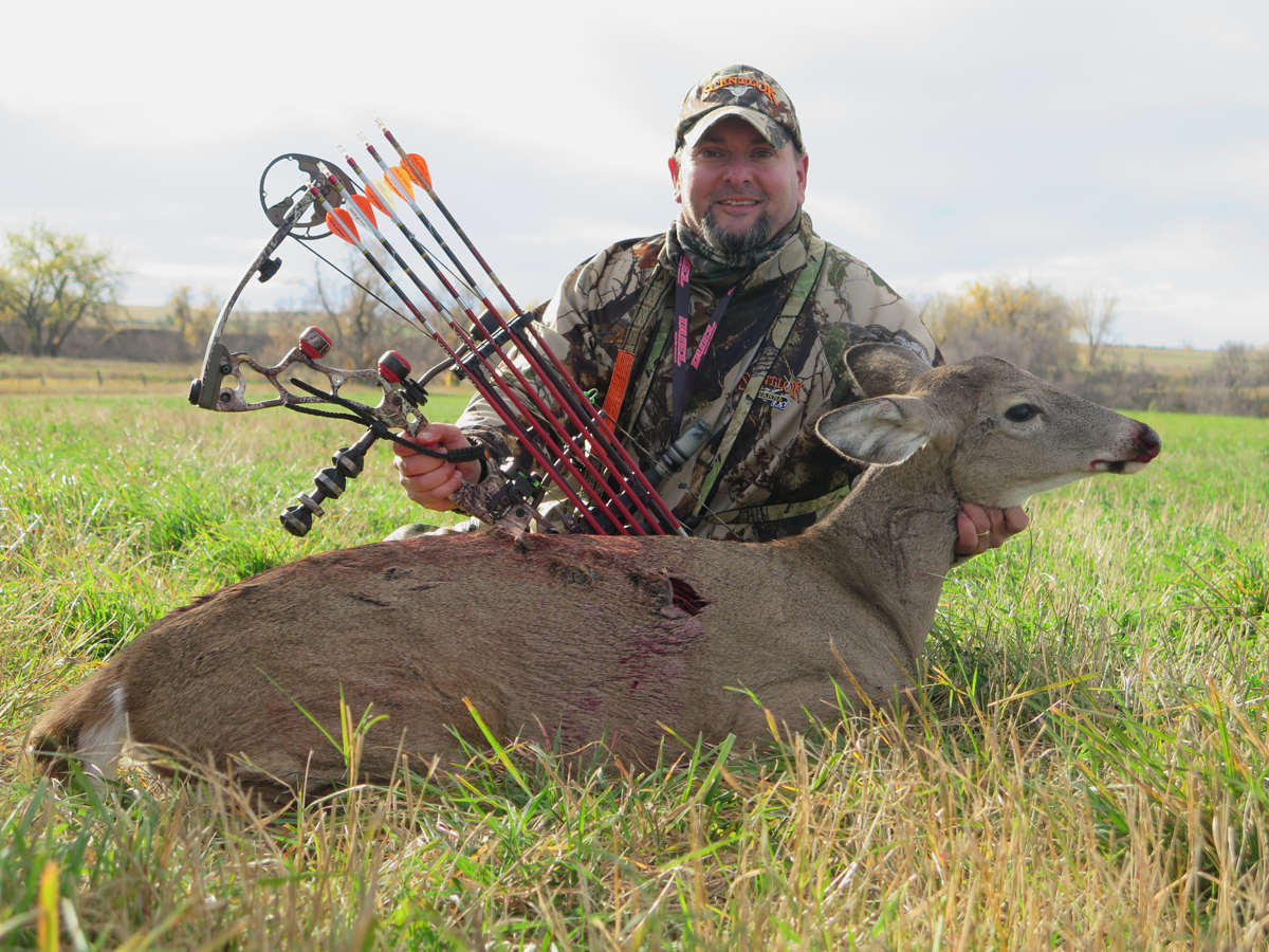 一个拿着复合弓和箭的弓箭猎人，坐在一头死白尾母鹿后面。
