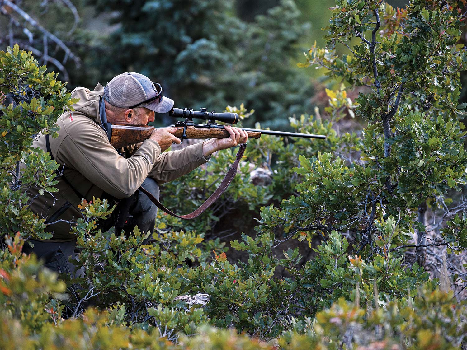 一个猎人站在灌木丛和掩蔽物之间，通过膛线镜观察，肩上举着步枪，准备开火。