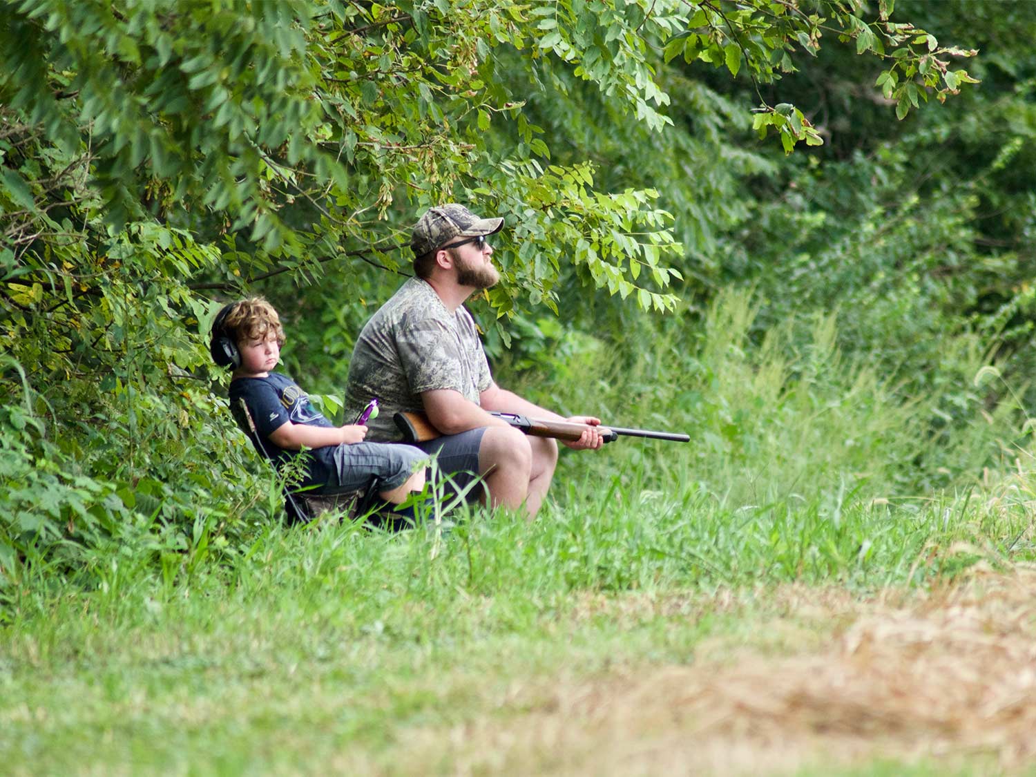 一个男人和一个小孩坐在田野的边缘去打猎。