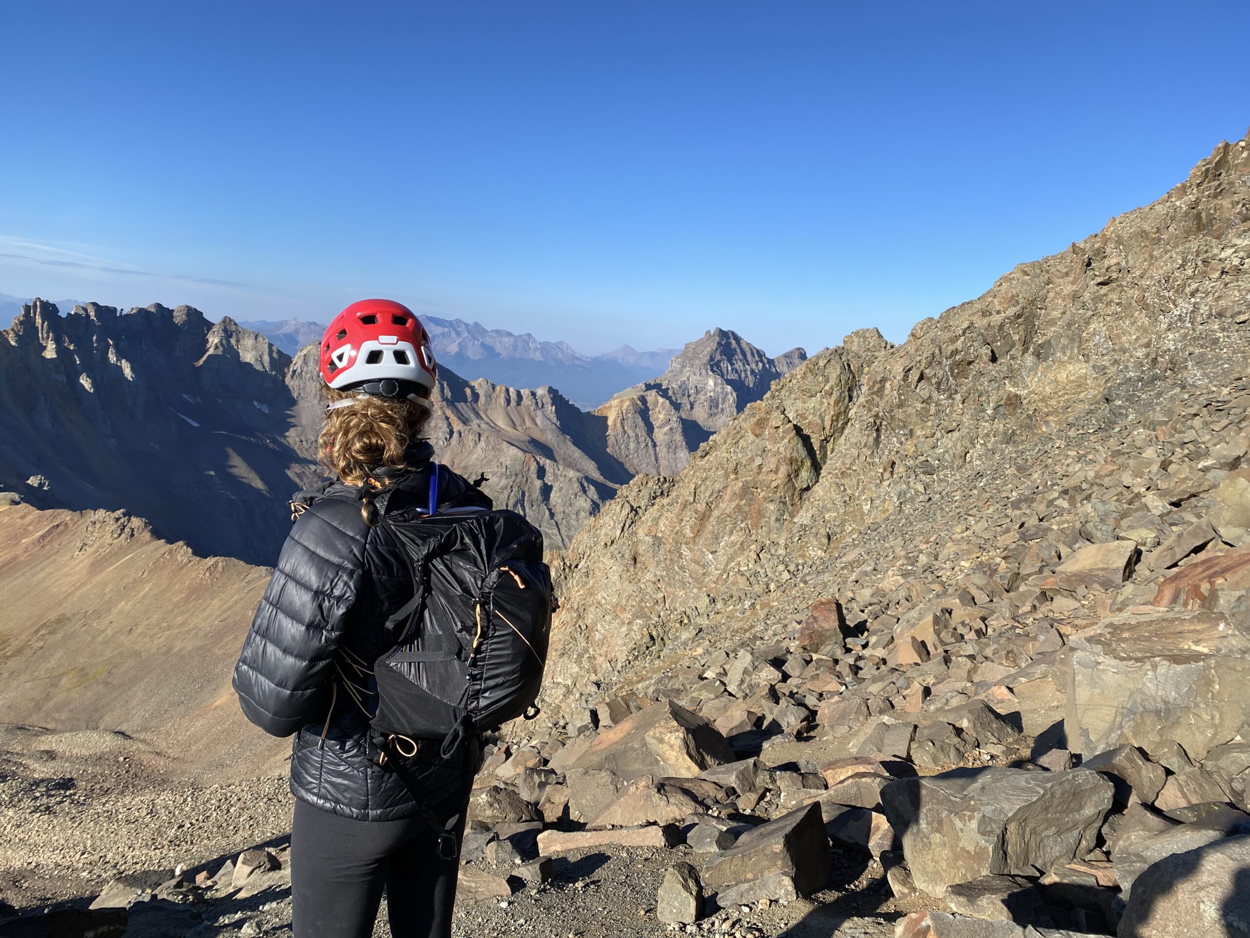 一个穿着黑色夹克、黑色背包、戴着红色登山头盔的女人俯瞰群山
